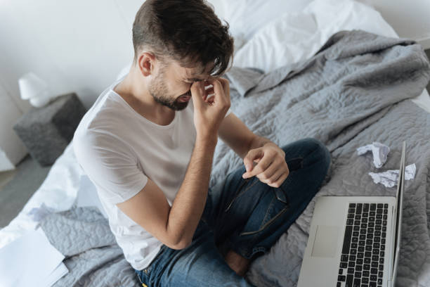 Inspiration crisis. Cheerless unhappy nice man sitting in front of the laptop and touching his bridge of the nose while trying to concentrate